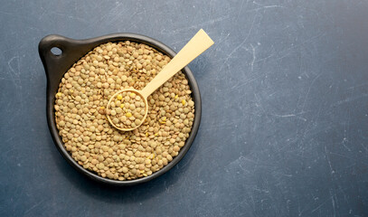 Bowl of raw brown lentils on a blue concrete background, with a wooden spoon decorating the plate