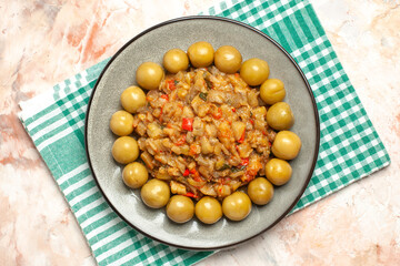 top view roasted eggplant salad and pickled plums on oval plate on turquoise white checkered tablecloth on nude background