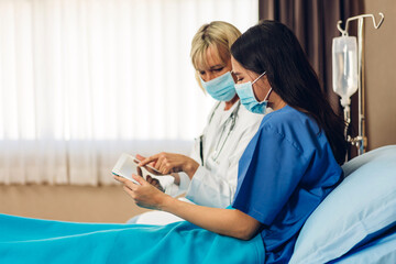 Senior woman doctor wearing protective mask with stethoscope service help support discussing and consulting talk to sick woman patient about checkup result information with tablet in hospital