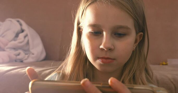 Little girl enjoys playing on smartphone phone in pink room art noise