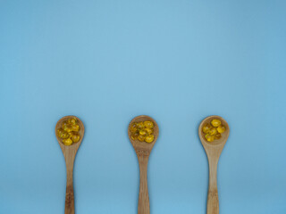 Bright yellow soft vitamin D tablets on wooden spoons on a light blue background with copy space. Immunity support in winter, lack of vitamin D. Doctor's recommendations. Top view, flat lay