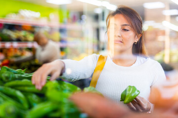 Positive woman picking ripe bell peppers at grocery supermarket