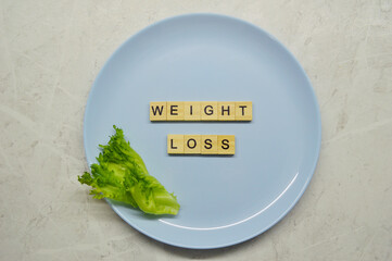 Phrase weight loss made of wooden letters on a blue plate with a leaf of lettuce