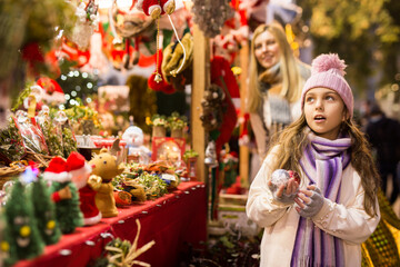 Surprised teenage girl looking at tree decorations at street christmas market