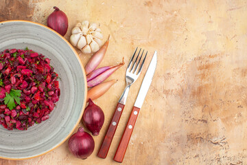 top close view of bowl of a red salad with greens on it on a wooden backgorund with a fork and knife on the side and vegetables at the side with free place for your text
