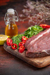 Side view of red meat on wooden cutting board and garlic green chopped pepper oil bottle lemon on dark background