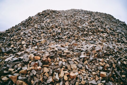 Pile of wet gravel or stone in construction site on sky background. - Powered by Adobe