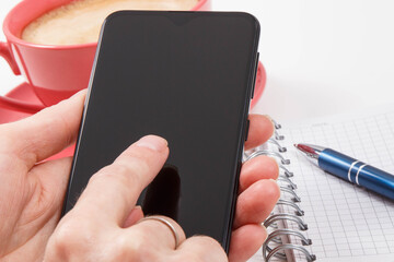 Hand of woman with mobile phone, coffee with milk and notepad for writing notes. White background