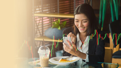 Close up excited young Asian businesswoman is watching a trading graph by her cell phone while while lunch time at canteen