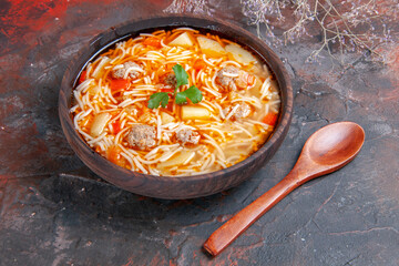 Close up view of delicious noodle soup with chicken in a brown bowl and spoon on the dark background