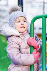 little girl in a knitted hat and warm jacket on a walk on a little girl in winter clothes is naughty on the playground. disobedient child. child manipulator