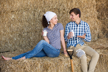 Naklejka na ściany i meble smiling young man and woman chatting and enjoying fresh milk in the hay