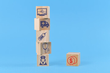 Concept for discrepancy between costs for medical treatments and funding depicted with wooden blocks with medical icons like nurse and ambulance and dollar sign