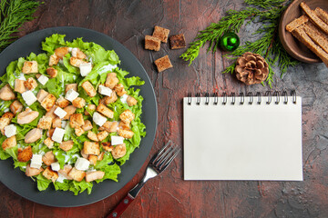 top view caesar salad on oval plate fork bowl with dried crust a notebook on dark red background