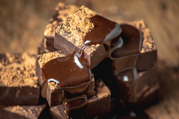 Delicious appetizing dark chocolate bars of a square shape are stacked in a tower and poured with liquid chocolate