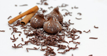 Trufas de chocolate con palitos de canela y virutas de chocolate sobre fondo blanco.