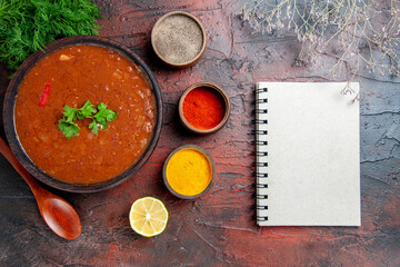 Classic tomato soup in a brown bowl different spices and notebook on mixed color table