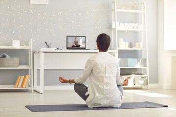 Woman sitting on fitness carpet and practicing meditation or yoga online using laptop