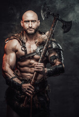 Fototapeta na wymiar Barbarian with bald head and grimy and bloody skin dressed in armour with fur posing in dark smokey background holding two handed double axe.