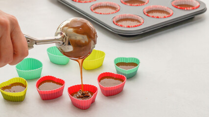 Chef pouring chocolate cake batter into  silicon heart-shaped mini molds. Chocolate cupcakes or...
