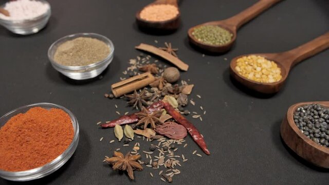 A spoonful of Sabut Urad Dal kept with other lentils with whole and powdered spices. Cooking with spices/masala various kind of legumes in an Indian kitchen against a black background
