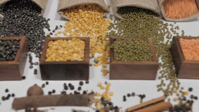 Raw pulses falling from gunny bag in front of wooden containers with Dal/lentils. An assortment of legumes - Moong(green)  Masoor(red)  Arhar(yellow)  Sabut Urad(black beans) with whole Indian spices