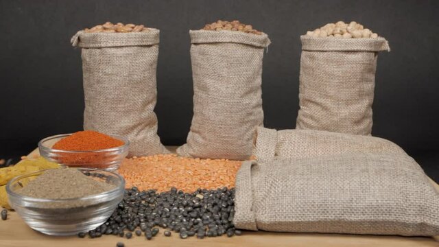 Rich protein source - Collection of lentils/dals/pulses in jute bags kept with powdered spices. Closeup view of sacks of Sabut Urad and Masoor Dal falling on a wooden table with other lentils  turm...