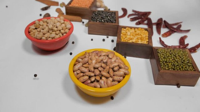 Different Dal/lentils in containers with whole spices and red chilies kept together. Closeup view of fresh-raw Indian pulses kept in wooden and plastic vessels against a white background