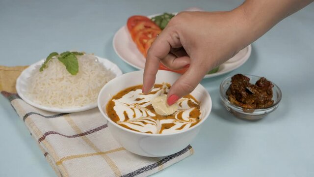 Famous Indian meal of steamed rice and dal makhani served with salad and pickle. Woman's hand putting a chunk of butter in the bowl of Dal Makhani decorated with fresh cream - a popular dish from I...
