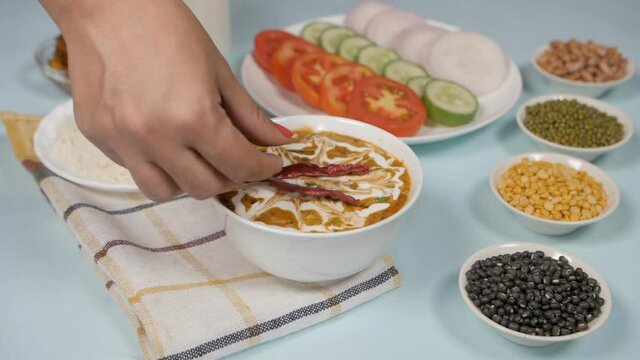 Female's hand putting dried red chilies on top of a fresh bowl of Dal Makhani. Various raw lentils  for preparing a popular dish (Dal Makhani) kept on a lunch / dinner table with rice  salad  butte...