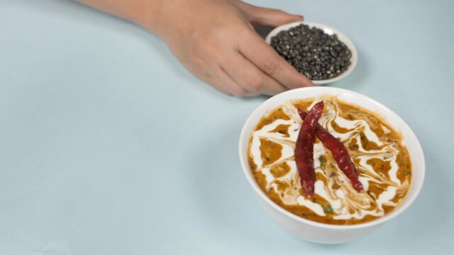 Human hand keeping a bowl of Sabut Urad Dal / black lentils with cooked Dal Makhani. Closeup shot of a popular Indian dish Dal / Daal Makhani - slow-cooked creamy pulses with Black lentils and Red ...