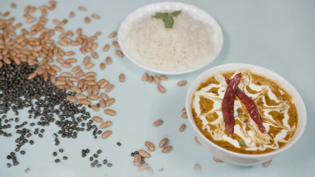 Black lentils / sabut urad dal and kidney beans / rajma dropping on a lunch table. Closeup shot of famous Indian meal of Dal Makhani cooked with black lentils and kidney beans served with plain ste...