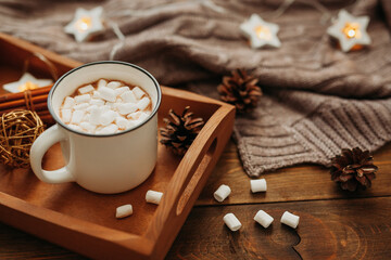 Cup of hot winter Christmas drink of chocolate or cocoa with marshmallows on a wooden tray in a cozy interior with a knitted blanket. Cozy winter holiday concept