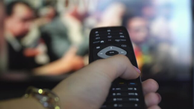 POV female hand holding a smart tv remote control changing tv channels