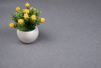 Artificial plastic flowers in white pot on gray background. Colors of year 2021 gray and illuminating yellow. Copyspace for text