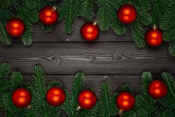Beautiful festive frame made of fir branches and red christmas balls on a dark wooden background. Copy space. Top view, flat lay