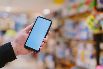 Mock-up technology. The guy holds a smartphone in his hands on the background supermarket.