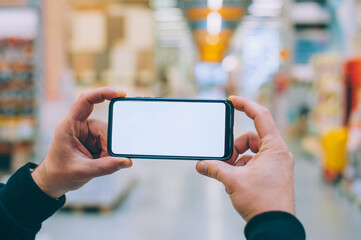 Mock-up technology. The guy holds a smartphone in his hands on the background supermarket.