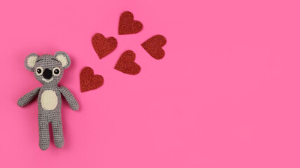Knitted toy koala and red hearts on a pink background