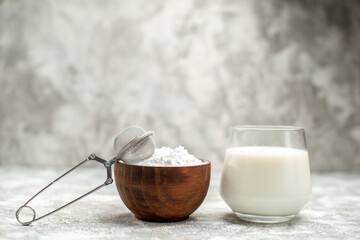 front view wooden bowl with powered sugar and a sieve a glass of milk on grey isolated background with copy space