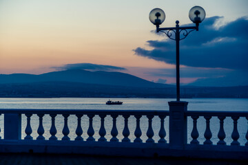 Silhouette of a balustrade with lanterns against the background of mountains. The ship sails on the sea. Blue sunset.