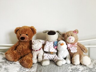 Assorted cuddly toys or teddy bears sitting on a cosy bed  in a row