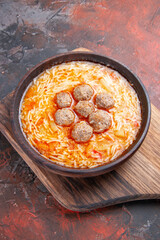 Vertical view of tasty meatballs soup with noodles on wooden cutting board on dark background