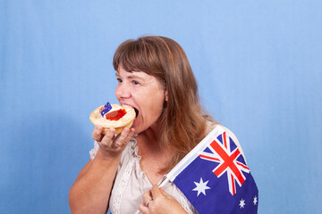 Middle aged woman eating a traditional meat pie with an Australian flag in her hand..