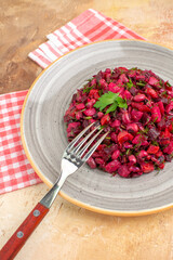 top close view of plate of a red salad with greens on it on a checked napkin and the fork on it on a wooden backgorund