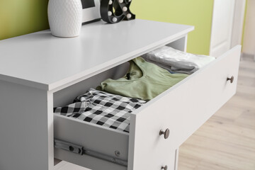 Modern chest of drawers with clothes in room