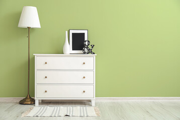 Modern chest of drawers with lamp near color wall in room