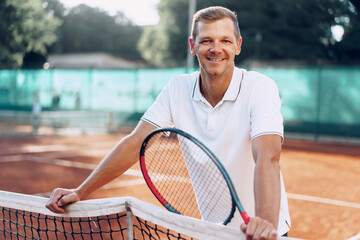 Portrait of positive male tennis player with racket standing at clay court