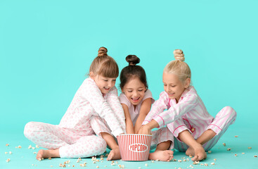 Cute little girls in pajamas eating popcorn on color background