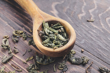 Spoon with dry green tea on wooden background